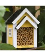 Bienenhotel Biholk Gelb von Wildlife Garden zwischen grünen Blättern im Garten, mit gelber Holzfassade, weißen Dachleisten und hohlen Bambusröhrchen.