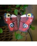 DecoButterfly Tagpfauenauge aus Holz von Wildlife Garden mit rotbraunen Flügeln, vier auffälligen Augenflecken und dunklen Flügelrändern zwischen grünen Blättern.