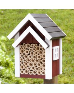 Bienenhotel Biholk Rot von Wildlife Garden auf einem Holzpfosten im grünen Garten, mit roter Holzfassade, weißen Dachleisten und hohlen Niströhren.