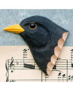 Kühlschrankmagnet Amsel aus Holz von Wildlife Garden mit schwarzem Gefieder, gelbem Schnabel und gelbem Augenring, fotografiert auf einem Notenblatt.