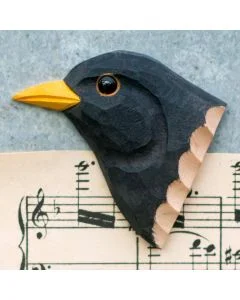 Kühlschrankmagnet Amsel aus Holz von Wildlife Garden mit schwarzem Gefieder, gelbem Schnabel und gelbem Augenring, fotografiert auf einem Notenblatt.