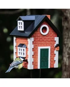 Kohlmeise an der Futteröffnung des Multiholk Brick Cottage von Wildlife Garden, einem Vogelhaus in roter Backsteinoptik mit grüner Tür und schwarzem Satteldach.