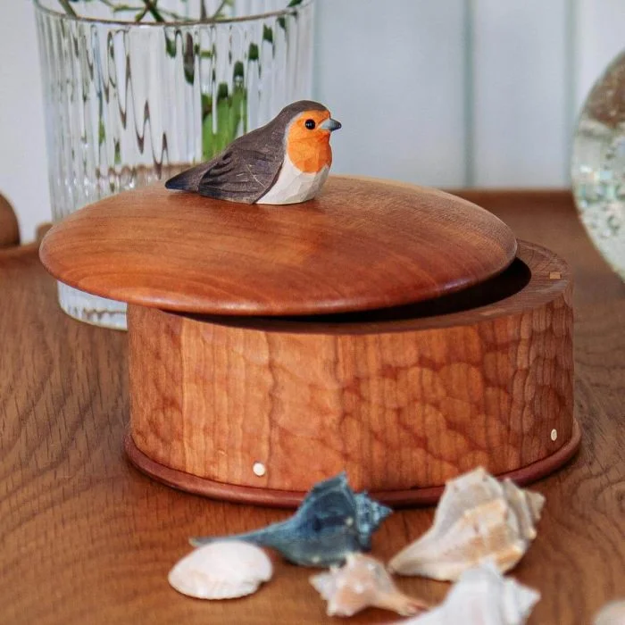 Runde Holzdose Rotkehlchen von Wildlife Garden mit geschnitzter Vogelfigur auf dem Deckel, dekoriert auf einem Holztisch mit Muscheln und Glasvase.