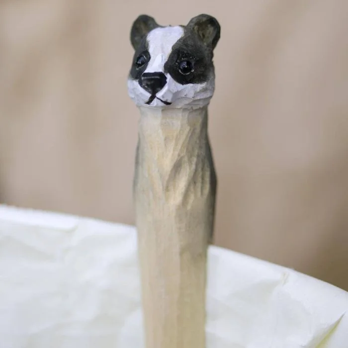 DecoClip Dachs von Wildlife Garden als dekorative Holz-Wäscheklammer mit schwarz-weißem Dachskopf, befestigt am Rand einer weißen Serviette.