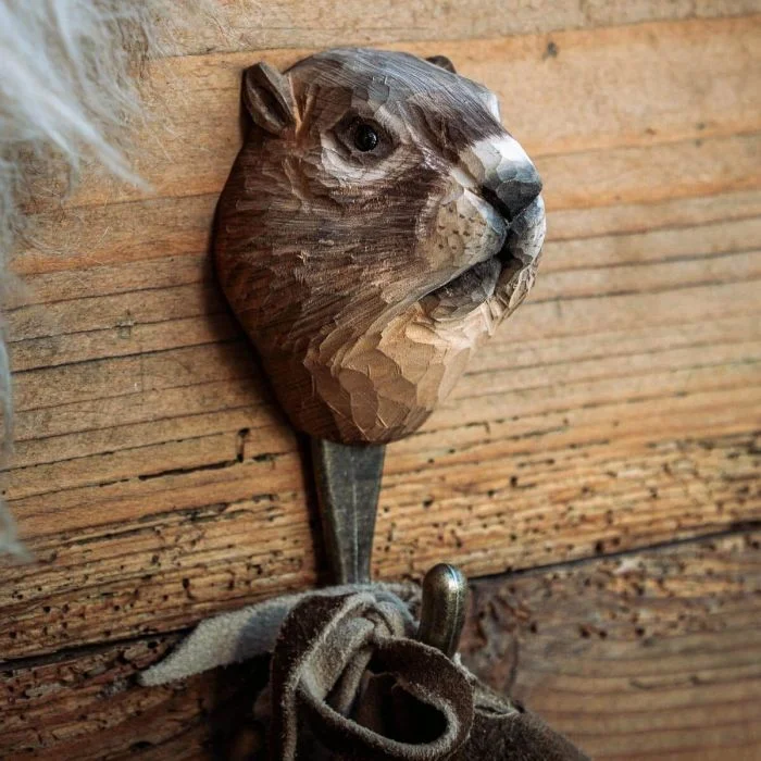 Kleiderhaken Alpenmurmeltier von Wildlife Garden an einer rustikalen Holzwand, mit geschnitztem braunem Murmeltierkopf und Stoffschlaufe am Metallhaken.