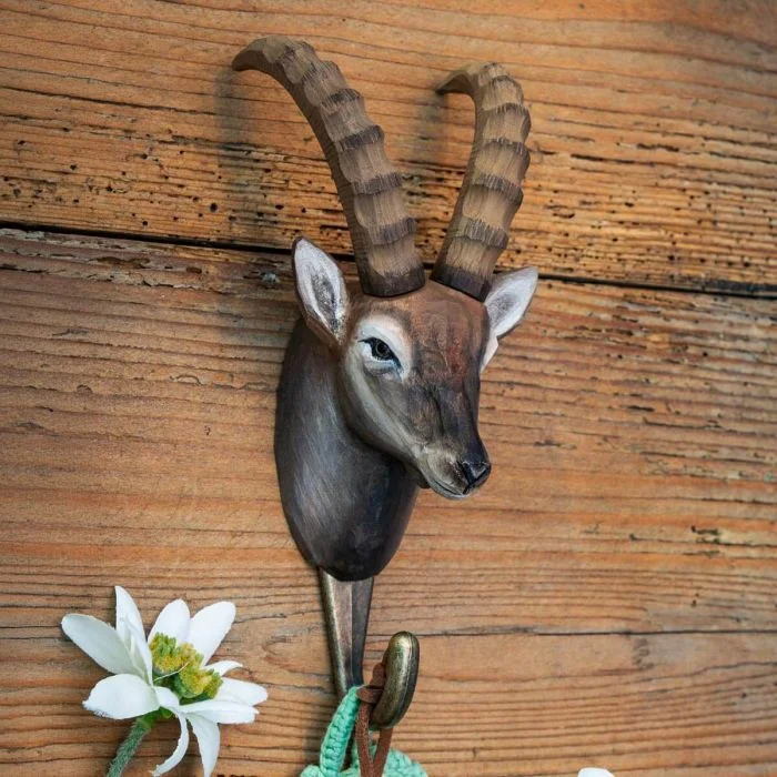 Kleiderhaken Alpensteinbock von Wildlife Garden an einer rustikalen Holzwand, mit braunem Steinbockkopf, langen gerippten Hörnern und Metallhaken.