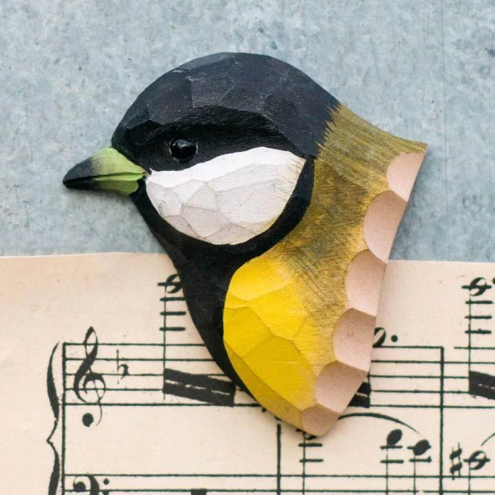 Kühlschrankmagnet Kohlmeise aus Holz von Wildlife Garden mit schwarzem Kopf, weißen Wangen und gelber Brust auf einem Notenblatt.