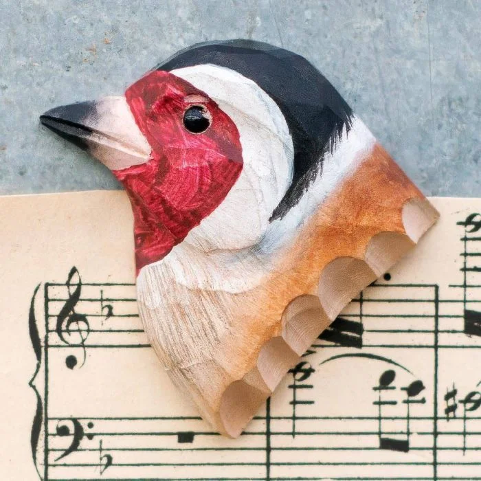 Kühlschrankmagnet Stieglitz aus Holz von Wildlife Garden mit roter Gesichtsmaske, schwarz-weißem Kopf und braunem Gefieder auf einem Notenblatt.